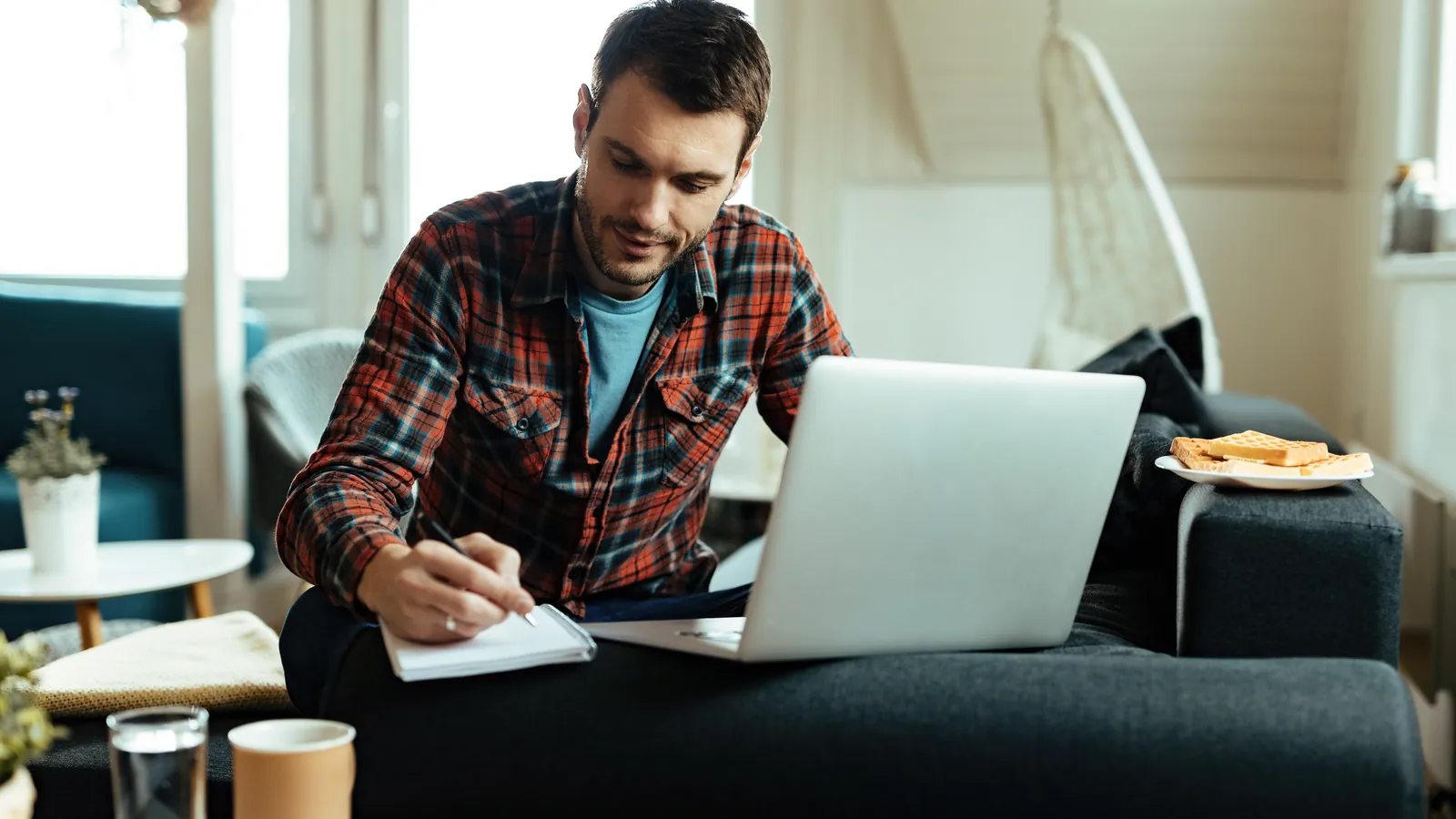 A business owner writing notes beside his laptop at home