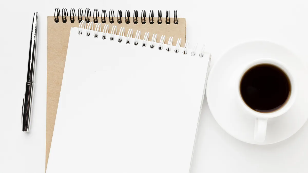 A blank notepad, a pen and a cup of coffee on a white desk
