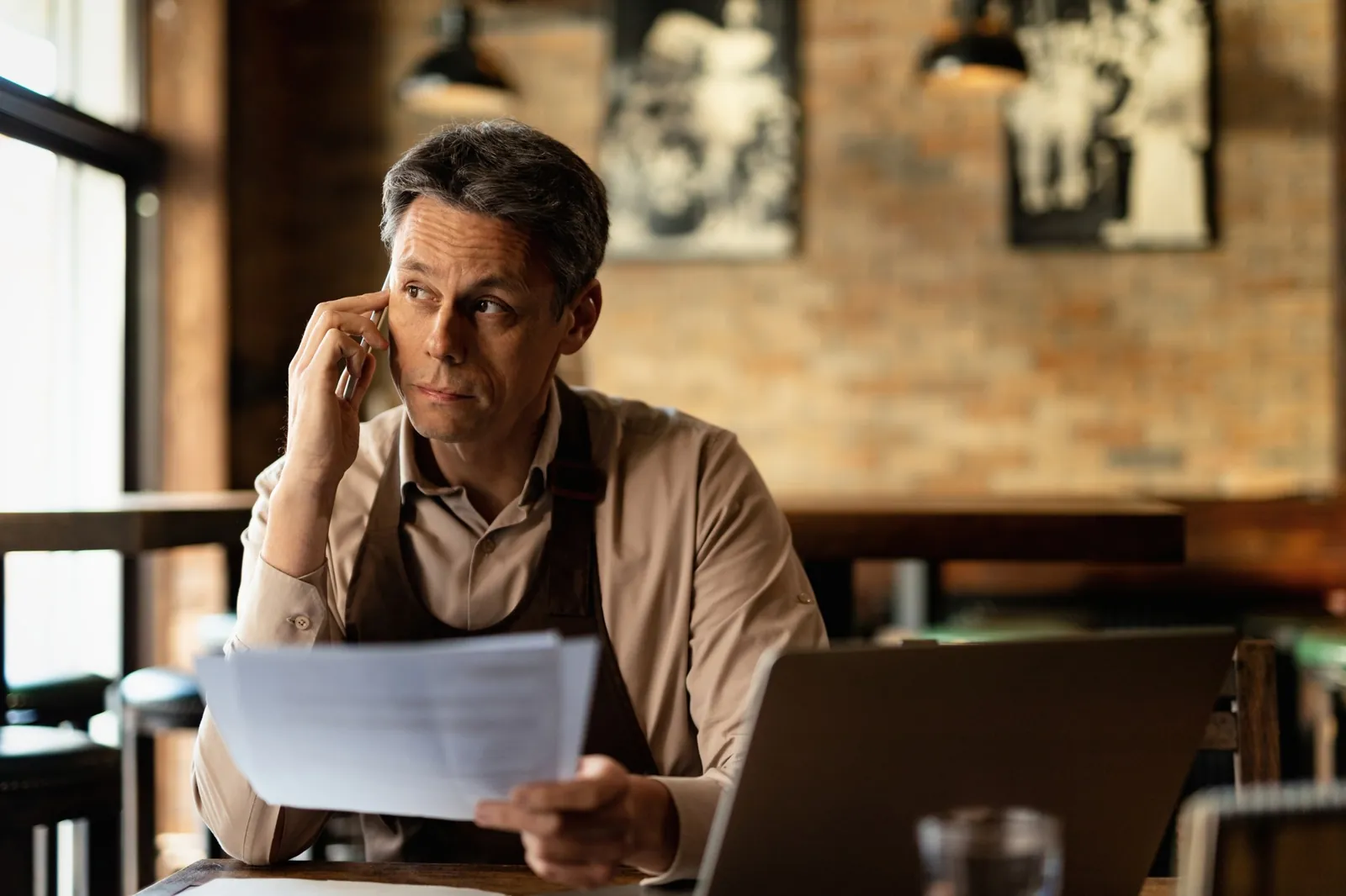 A café owner on the phone going through paperwork at a table after hours