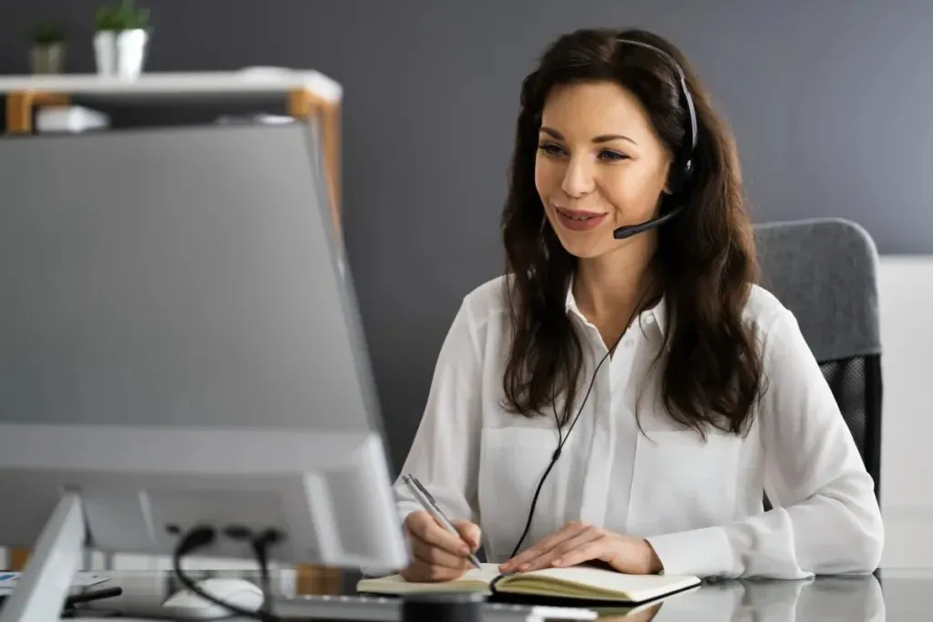 A smiling assistant with a headset taking notes at her computer