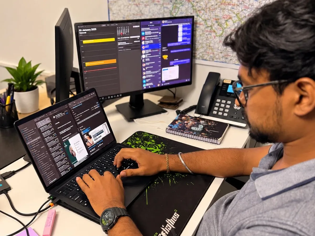 A business assistant typing at a laptop, a calendar and inbox open on the monitor behind
